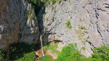 Bereketli yeşil ağaçlar ve ormanlarla çevrili kayalık bir uçurumdan şelalenin havadan çekilmiş videosu güneşli bir yaz gününde FPV insansız hava aracıyla ağır çekimde çekildi..
