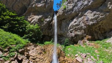 Bereketli yeşil ağaçlar ve ormanlarla çevrili kayalık bir uçurumdan şelalenin havadan çekilmiş videosu güneşli bir yaz gününde FPV insansız hava aracıyla ağır çekimde çekildi..