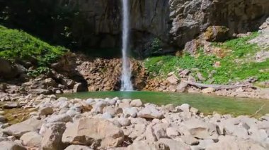 Bereketli yeşil ağaçlar ve ormanlarla çevrili kayalık bir uçurumdan şelalenin havadan çekilmiş videosu güneşli bir yaz gününde FPV insansız hava aracıyla ağır çekimde çekildi..