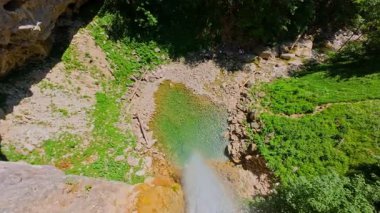 Bereketli yeşil ağaçlar ve ormanlarla çevrili kayalık bir uçurumdan şelalenin havadan çekilmiş videosu güneşli bir yaz gününde FPV insansız hava aracıyla ağır çekimde çekildi..