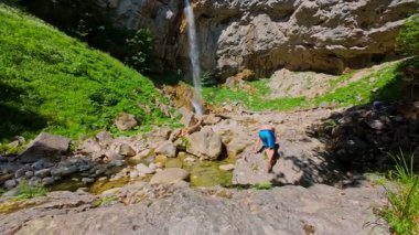 Güneşli bir günde yemyeşil orman ve kayalarla çevrili temiz bir dağ nehrinde yüzen bir kadının FPV drone görüntüsü. Vahşi doğada yaz kaçamağı, macera ve seyahat için ideal.. 