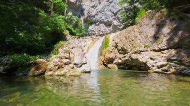 Bereketli yeşil ağaçlar ve ormanlarla çevrili kayalık bir uçurumdan şelalenin havadan çekilmiş videosu güneşli bir yaz gününde FPV insansız hava aracıyla ağır çekimde çekildi..