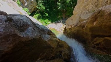 Bereketli yeşil ağaçlar ve ormanlarla çevrili kayalık bir uçurumdan şelalenin havadan çekilmiş videosu güneşli bir yaz gününde FPV insansız hava aracıyla ağır çekimde çekildi..
