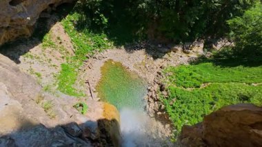 Bereketli yeşil ağaçlar ve ormanlarla çevrili kayalık bir uçurumdan şelalenin havadan çekilmiş videosu güneşli bir yaz gününde FPV insansız hava aracıyla ağır çekimde çekildi..