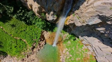 Bereketli yeşil ağaçlar ve ormanlarla çevrili kayalık bir uçurumdan şelalenin havadan çekilmiş videosu güneşli bir yaz gününde FPV insansız hava aracıyla ağır çekimde çekildi..