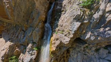 Bereketli yeşil ağaçlar ve ormanlarla çevrili kayalık bir uçurumdan şelalenin havadan çekilmiş videosu güneşli bir yaz gününde FPV insansız hava aracıyla ağır çekimde çekildi..