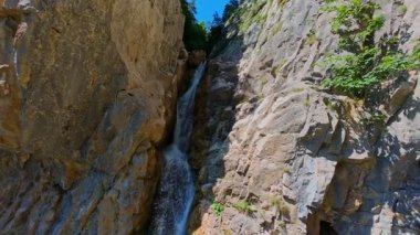 Bereketli yeşil ağaçlar ve ormanlarla çevrili kayalık bir uçurumdan şelalenin havadan çekilmiş videosu güneşli bir yaz gününde FPV insansız hava aracıyla ağır çekimde çekildi..