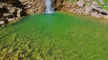Bereketli yeşil ağaçlar ve ormanlarla çevrili kayalık bir uçurumdan şelalenin havadan çekilmiş videosu güneşli bir yaz gününde FPV insansız hava aracıyla ağır çekimde çekildi..