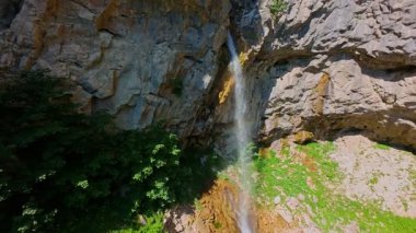 Bereketli yeşil ağaçlar ve ormanlarla çevrili kayalık bir uçurumdan şelalenin havadan çekilmiş videosu güneşli bir yaz gününde FPV insansız hava aracıyla ağır çekimde çekildi..