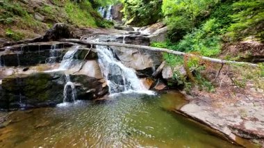 Bereketli yeşil ormanlarda kayaların üzerinden akan güzel bir şelalenin havadan çekilmiş videosu, temiz su akıntısı olan manzaralı doğa manzarası, rahatlama ve macera için gidilecek yer. Sinematik ağır çekim