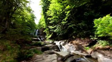 Bereketli yeşil ormanlarda kayaların üzerinden akan güzel bir şelalenin havadan çekilmiş videosu, temiz su akıntısı olan manzaralı doğa manzarası, rahatlama ve macera için gidilecek yer. Sinematik ağır çekim