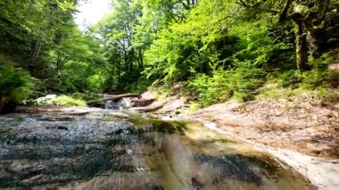 Bereketli yeşil ormanlarda kayaların üzerinden akan güzel bir şelalenin havadan çekilmiş videosu, temiz su akıntısı olan manzaralı doğa manzarası, rahatlama ve macera için gidilecek yer. Sinematik ağır çekim