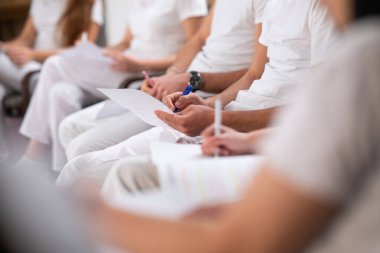 Profesyonel bir eğitim ve eğitim sırasında sağlık ve terapi kursunda elinde kalem tutan ve not defterine notlar yazan bir öğrenciyi kapatın..