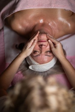 Profesyonel bir terapist göğüs masajı yaparken olgun bir kadının havluyla tedavi yatağına uzanması. Rahatlamayı vurgulayan spa sağlığı ve güzellik tedavi kavramı