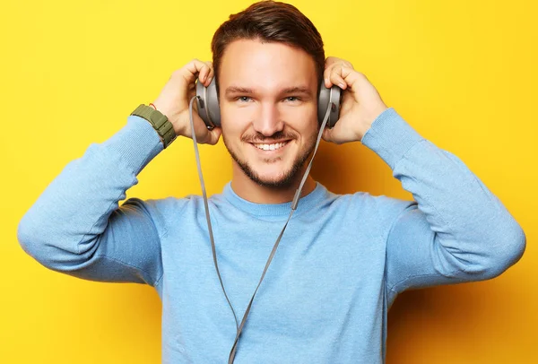 Estilo de vida y el concepto de la gente: Feliz joven escuchando música con auriculares sobre fondo amarillo —  Fotos de Stock