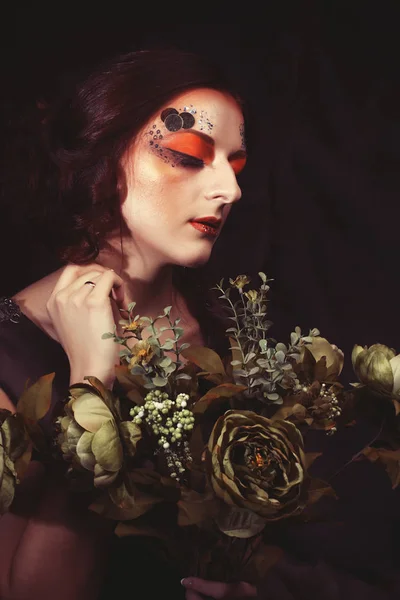 Крупним планом портрет рудоволоса жінка з яскравим креативним макіяжем, що тримає сухі квіти — стокове фото