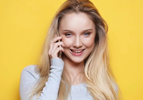 Portrait of young, happy woman talking on phone looking at camera, over yellow background — Stock Photo, Image