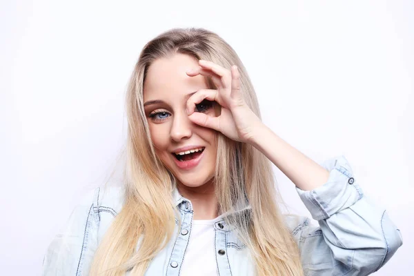 Estilo de vida e conceito de pessoas - Happy excited young woman looking through hole made of her fingers over white background — Fotografia de Stock