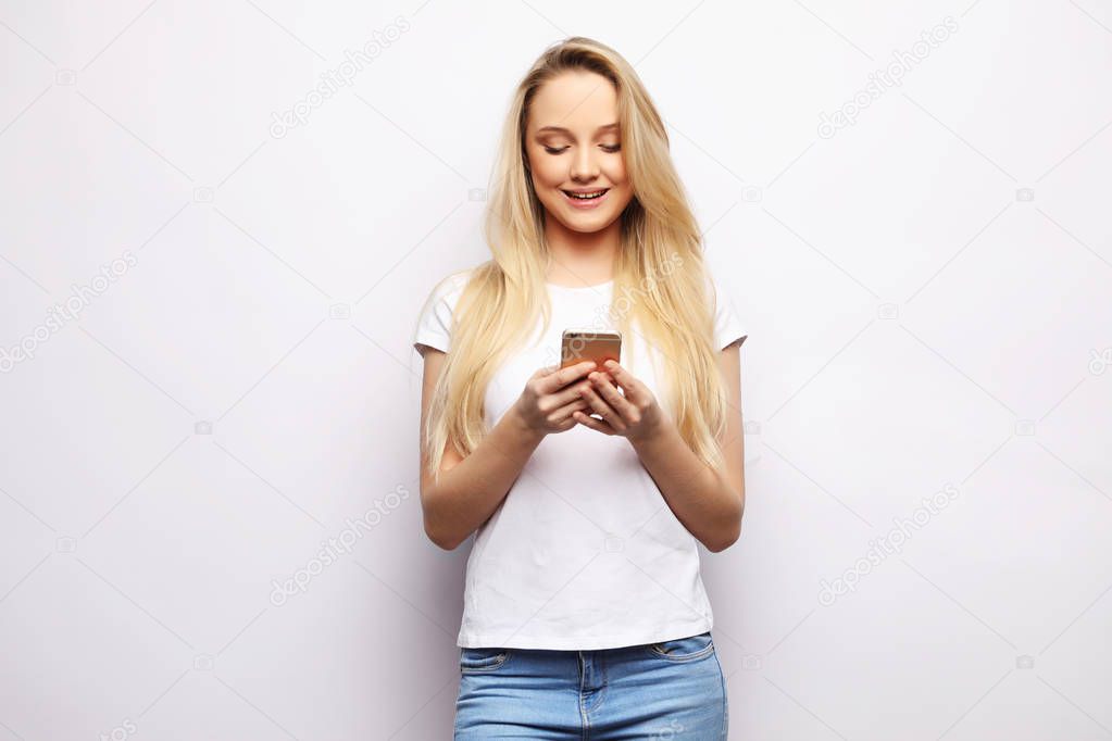 Pretty blond woman with long hair holds modern smart phone, recieves unexpcted message from friend, reads reminder