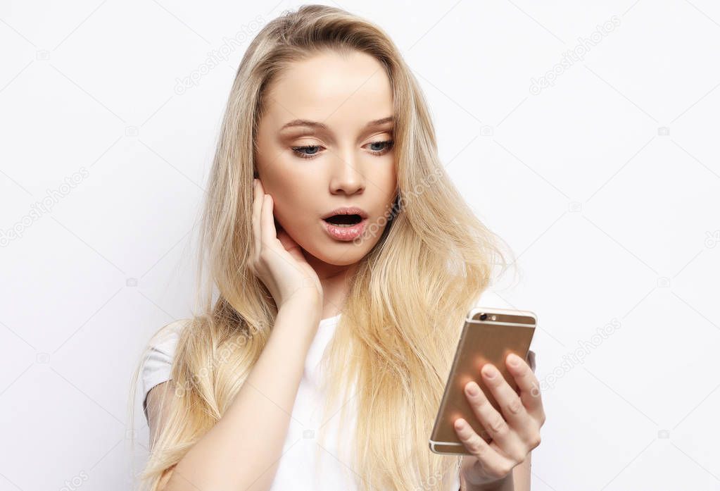 Shocking message. Surprised young blond hair woman holding mobile phone