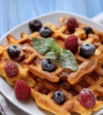 Taze sapılmak ve beyaz tabak, mavi ahşap zemin üzerine pudra şekeri ile geleneksel Belçika Waffle.