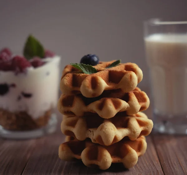 Buen desayuno. Gofres belgas con arándanos, un vaso de leche y granola con frambuesas sobre mesa de madera . — Foto de Stock