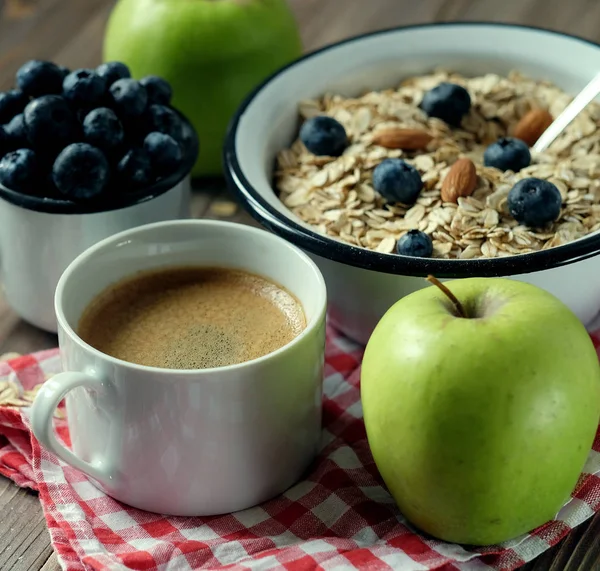 Ein gesundes Frühstück ist ein guter Start in einen neuen Tag. Haferbrei, Kaffee, Apfel, Beeren und Nüsse auf einem Holztisch. — Stockfoto