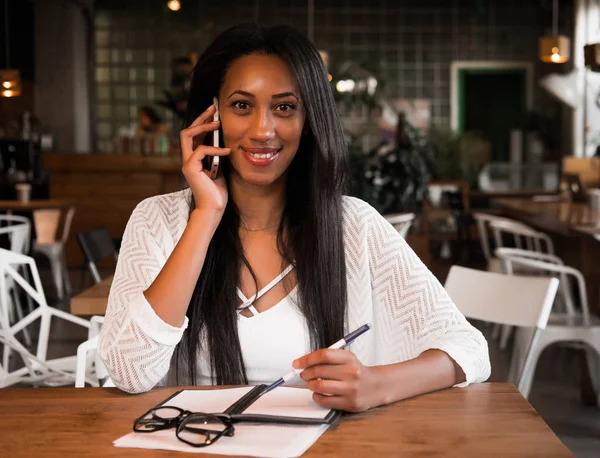 Yapılacaklar listesi yazmak ve getting haber Smartphone'da neşeli afro Amerikalı kız. Gülümseyen öğrenci ödev iyi haber üstünde hareket eden telefon ile bildirim okurken