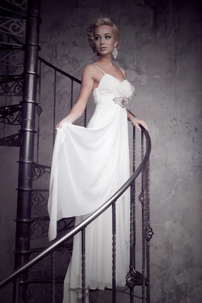 Beyaz elbiseli güzel genç gelin bir döner merdiven üzerinde duruyor. Düğün kavramı.