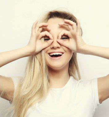 Yaşam tarzı ve insan konsepti - Mutlu heyecanlı genç kadın beyaz arka planda parmaklarından oluşan delikten bakıyor, yakın plan