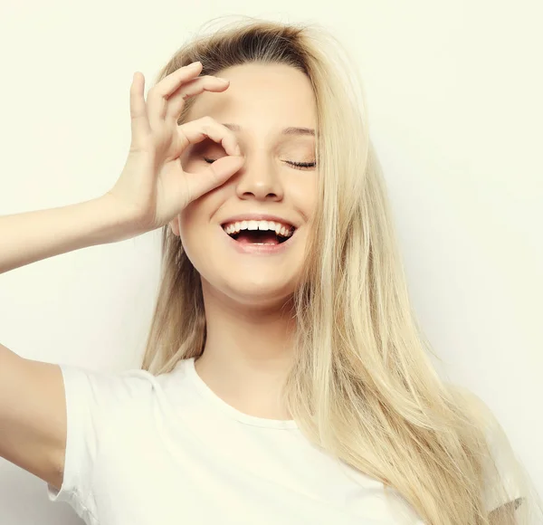 Lifestyle and people concept - Χαρούμενη ενθουσιασμένη νεαρή γυναίκα που κοιτάζει μέσα από μια τρύπα φτιαγμένη από τα δάχτυλά της πάνω από λευκό φόντο — Φωτογραφία Αρχείου