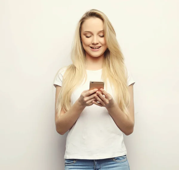Shocking message. Surprised young blond hair woman holding mobile phone and staring at it while standing against white background.