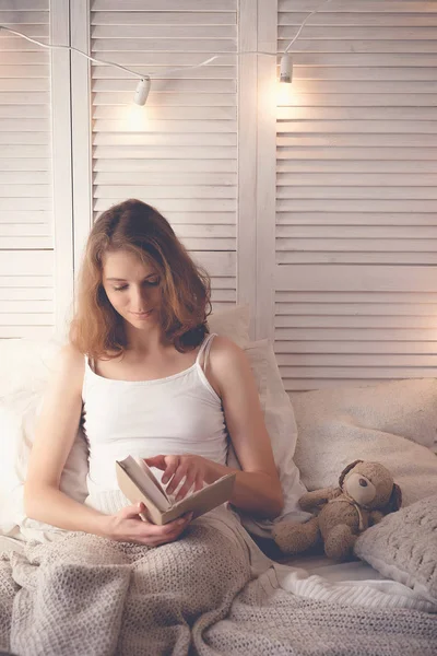 Styl życia i ludzi koncepcja: młody blond kobieta leżąc w łóżku podczas czytania książki, ciepły dźwięk — Zdjęcie stockowe