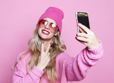 pembe arka plan üzerinde pinkl giyim eşyası Smartphone cep telefonu ile kendi kendine portre serin kız alarak fotoğraf yapar