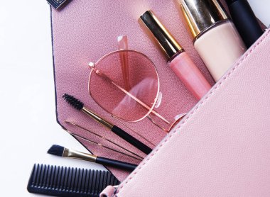 Moda konsepti: Pembe deri kadın çantasının bembeyaz arka planda kozmetik ve aksesuarlarla açılışı.