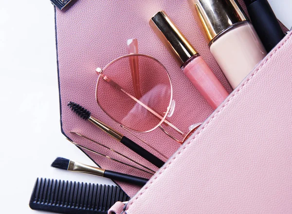 Modekonzept: Flache Damentasche aus rosa Leder mit Kosmetik und Accessoires auf weißem Hintergrund. — Stockfoto