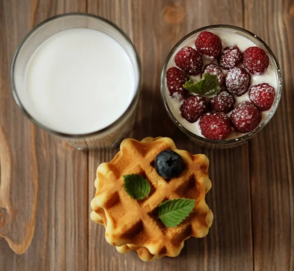 Feliz desayuno. Una taza pequeña con arándanos, un vaso de leche y granola con frambuesas . — Foto de Stock