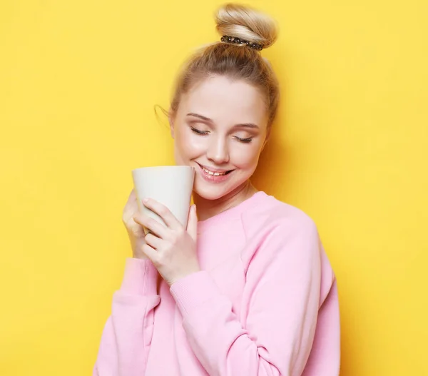 Jovem loira segurando xícara branca com chá ou café, estilo de vida e conceito de comida. Fundo amarelo . — Fotografia de Stock