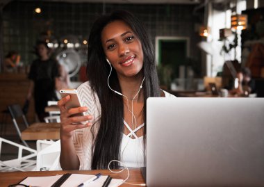 Yaşam tarzı ve insan konsepti: cep telefonu ve dizüstü bilgisayar kullanarak bir kafede mutlu bir Afrikalı kadının portresi