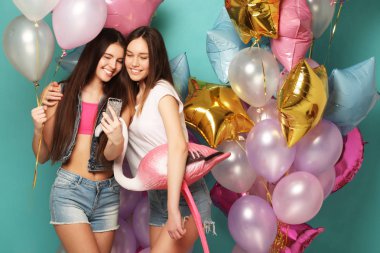 Partiye hazırız. Havalı yaz kıyafetleri içinde iki kız kağıt bardaklar ve hava balonları. Doğum günlerini kutluyorlar. Mavi arka plan..