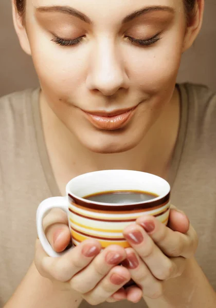 Portrait of a beautiful woman with a cup of coffee standing on the beige background — Stock Photo, Image