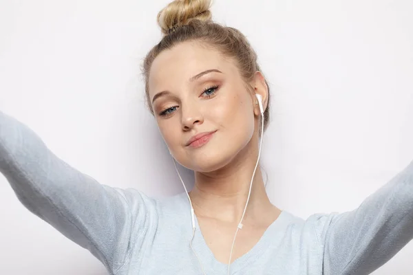 Blond meisje in koptelefoon luisteren muziek nemen foto maakt Zelfportret op smartphone een casual kleding dragen op witte achtergrond — Stockfoto
