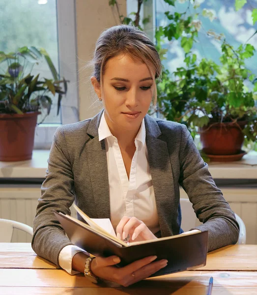 Молодая деловая женщина сидит за столом в кафе и читает книгу . — стоковое фото