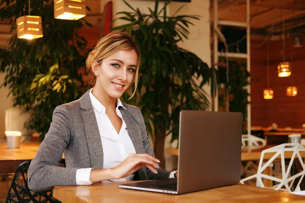 Gente y concepto de negocio: joven atractiva mujer de negocios sentada en un café con una computadora portátil — Foto de Stock