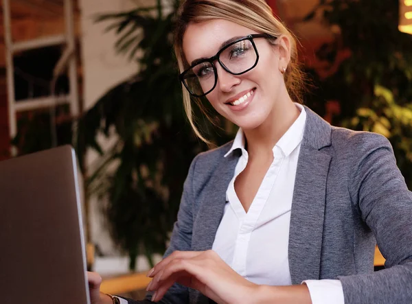 Gente y concepto de negocio: joven atractiva mujer de negocios sentada en un café con una computadora portátil — Foto de Stock