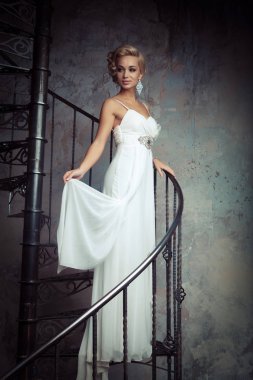 Beyaz elbiseli güzel genç gelin bir döner merdiven üzerinde duruyor. Düğün kavramı.