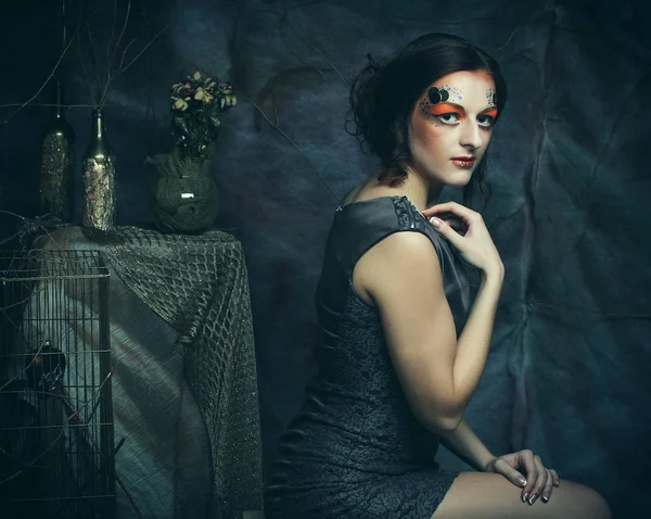 Joven modelo mujer con creativo maquillaje sentado en un taburete en la decoración de drama —  Fotos de Stock