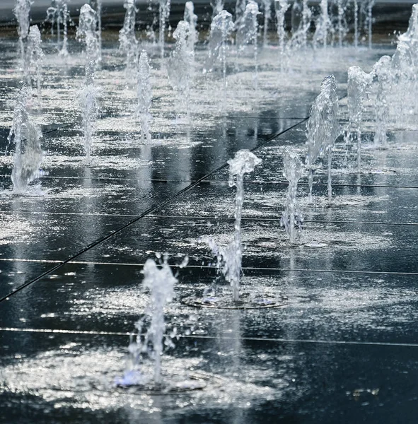 Pequeña fuente hermosa en el aire libre, en la calle. Gotas de agua, chorros de agua congelados en el aire en vuelo contra el telón de fondo . — Foto de Stock