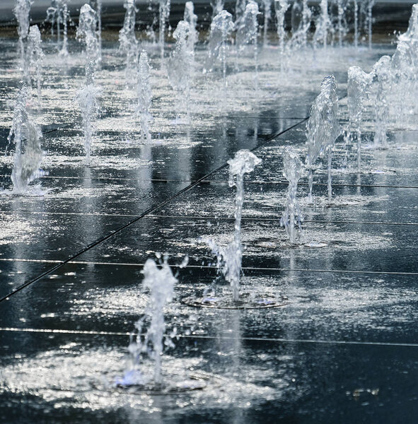 small beautiful fountain in the open air, on the street. Drops of water, jets of water frozen in the air in flight against the backdrop.