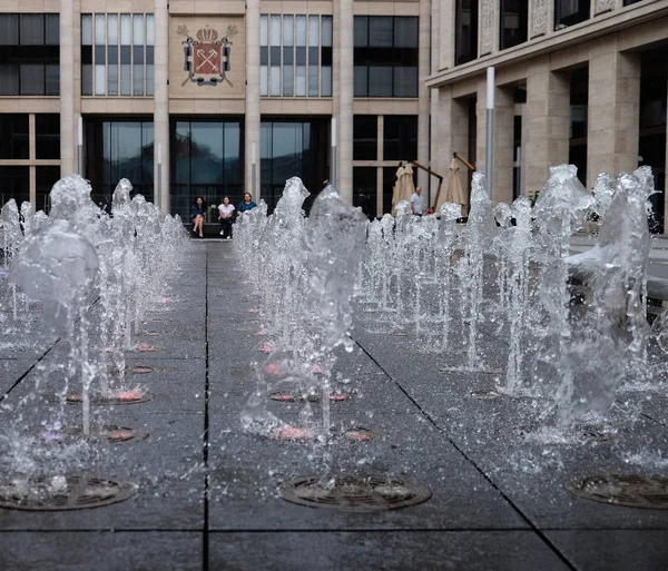 Pequeña fuente hermosa en el aire libre, en la calle. Gotas de agua, chorros de agua congelados en el aire en vuelo contra el telón de fondo . — Foto de Stock